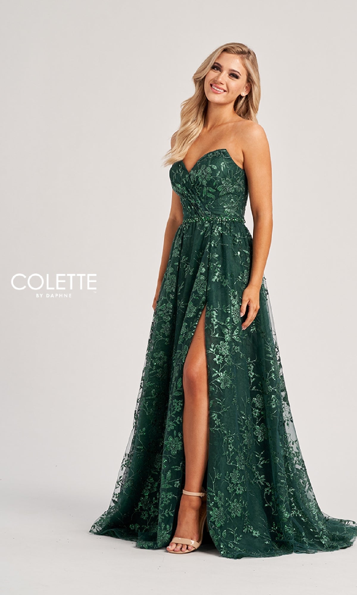 Woman in the Colette CL8260 long prom dress—strapless, dark green with a floral pattern and high slit—stands smiling against a plain light background.